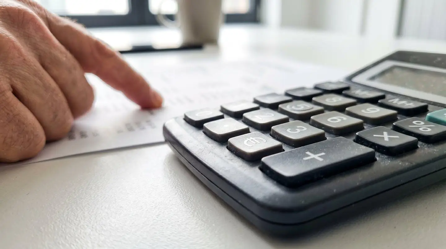 Gros plan d'une calculatrice financière avec le symbole euro visible, posée sur un bureau moderne, avec une main floue pointant vers un document dont le texte est totalement illisible